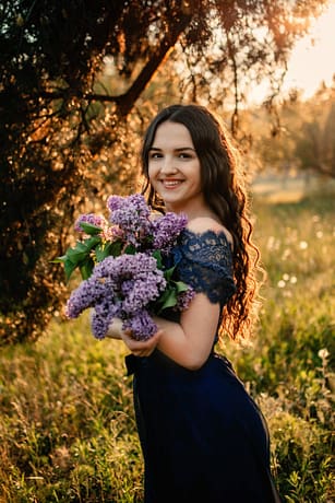 Party graduation prom fairytale concept. Beautiful brunette young woman in blue prom dress with lilac bouquet on nature background. Outdoor romantic portrait of brunette girl in long evening dress.